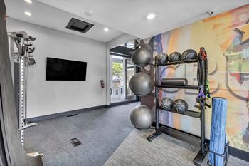A gym room with a television, exercise balls, and a rack of resistance bands.